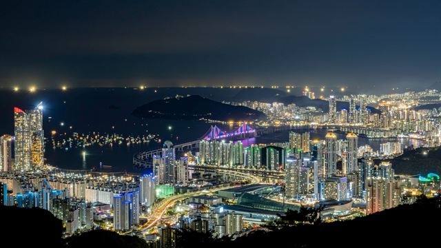 Busan at night from above, illuminated high-rises around Gwangalli with Gwangan Bridge lit in purple