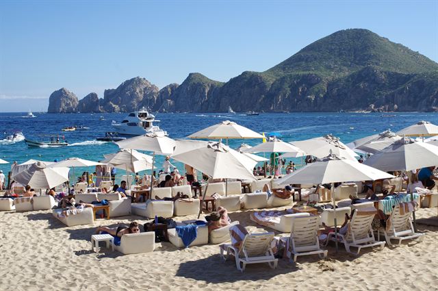 Crowded Medano Beach umbrellas and boats with the Land's End rock arch headland beyond, Cabo San Lucas