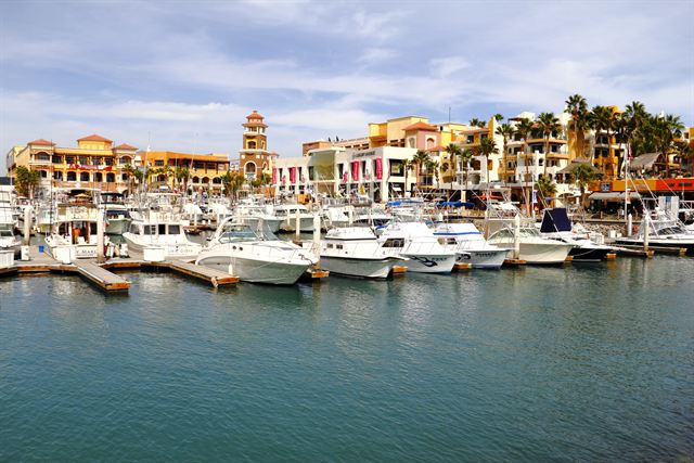 Yachts in Cabo San Lucas marina in front of colorful hillside resort buildings