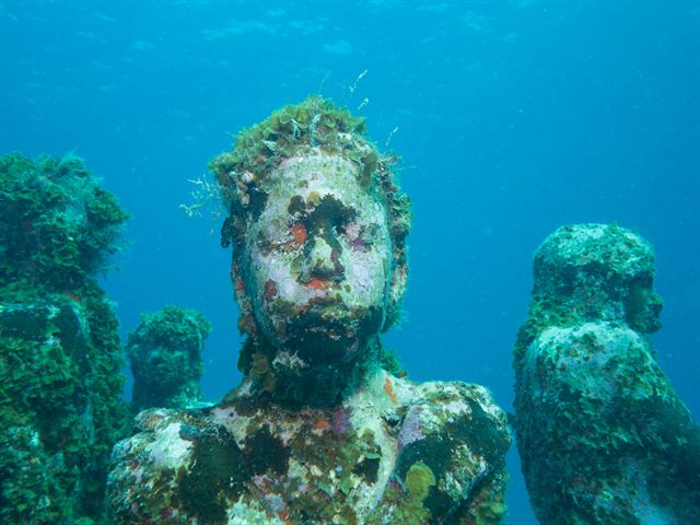 Coral-encrusted statues of Cancun's underwater museum (MUSA) in clear blue-green water