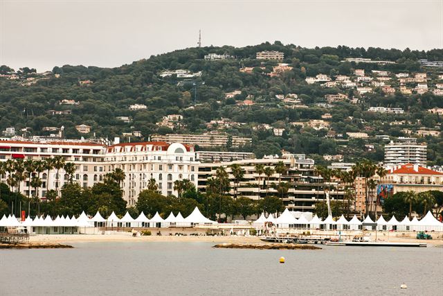 Cannes waterfront on the Croisette with beach tents, grand hotels and green hills behind
