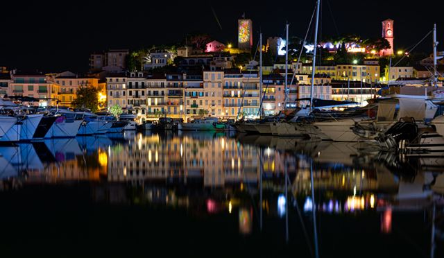 Cannes Old Port at night with illuminated Le Suquet and yachts reflected in the harbor