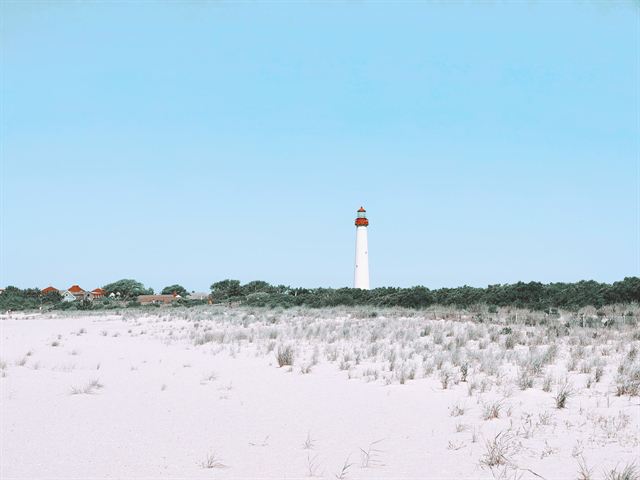 Cape May Lighthouse rising beyond white sand dunes under a clear blue sky in Cape May, New Jersey