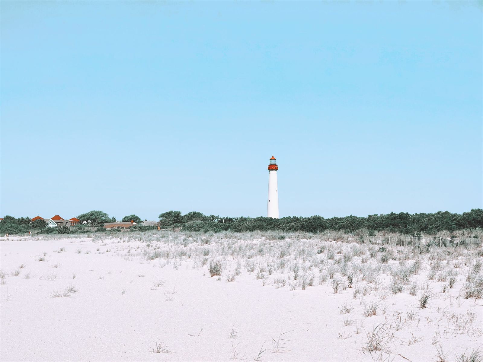 Cape May Lighthouse rising beyond white sand dunes under a clear blue sky in Cape May, New Jersey