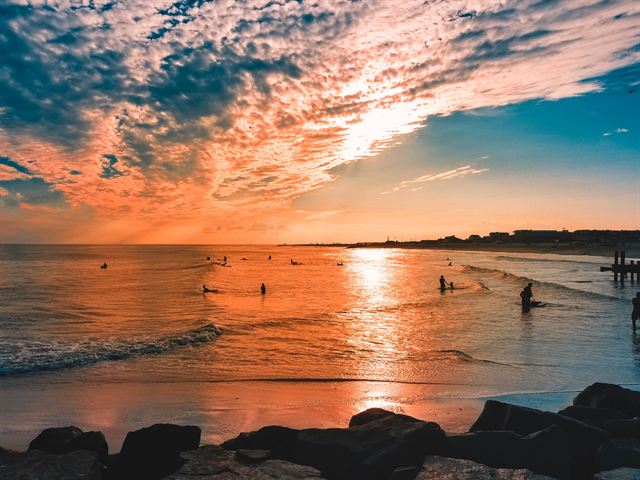 Vivid orange sunset reflected on the water at Cape May beach with rock jetty silhouettes