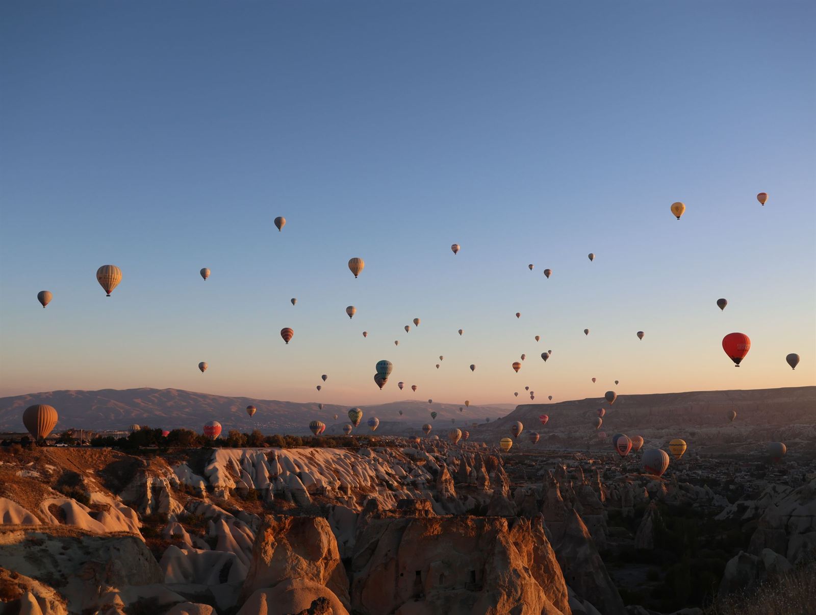 Dozens of hot air balloons drifting over Cappadocia's eroded valleys at sunrise