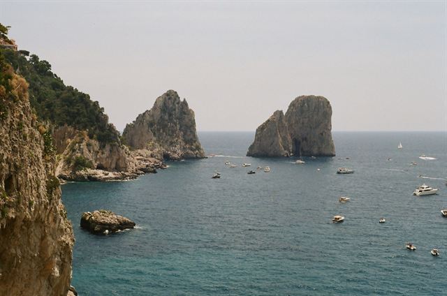Faraglioni sea stacks off Capri with boats on calm water beside steep green cliffs