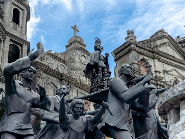 Bronze sculptures of the Heritage of Cebu Monument with a colonial church facade behind in Cebu City