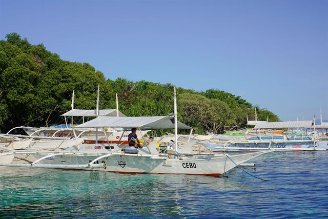 White outrigger bangka boats marked CEBU moored in clear turquoise water below green hills