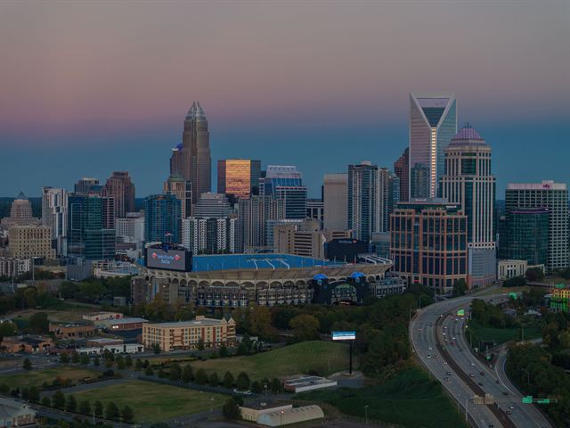 Charlotte skyline with Bank of America Corporate Center and Bank of America Stadium beside the freeway at dusk