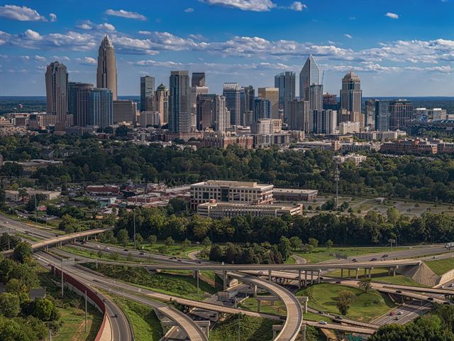 Uptown Charlotte skyscrapers rising above green trees and looping highway interchanges on a sunny day