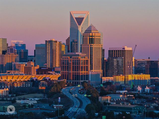Duke Energy Center and Uptown Charlotte towers glowing in warm sunset light under a pink sky