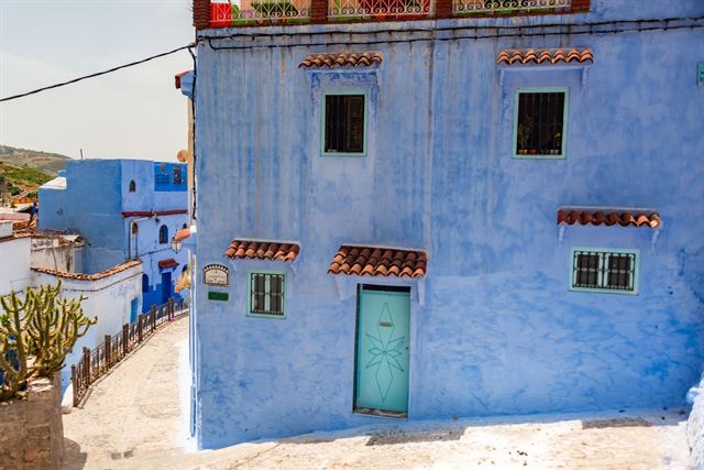 Blue-painted house with tiled window awnings on a sloping lane in Chefchaouen, Morocco