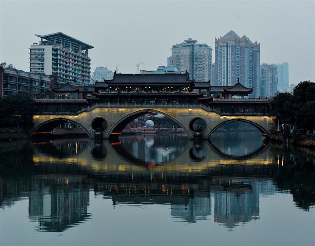 Anshun Bridge's arches and pavilion roof reflected in the Jin River beneath Chengdu high-rises