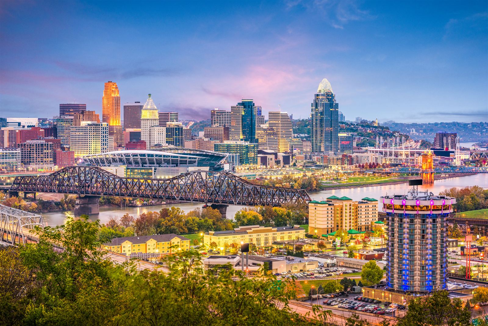 Cincinnati skyline at dusk across the Ohio River with bridges and hillside trees, Ohio