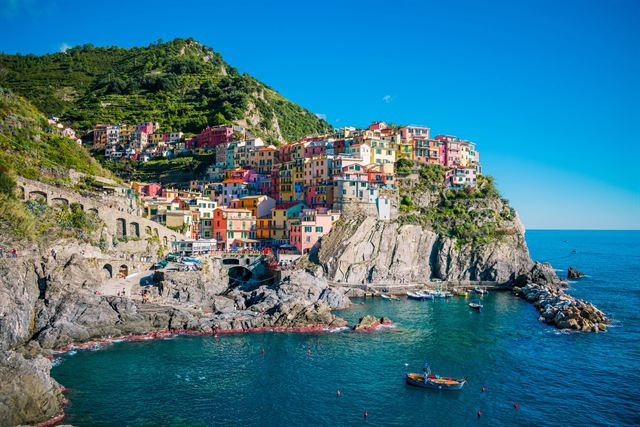 Manarola's colorful cliffside houses above a turquoise cove on the Cinque Terre coast, green terraced hills behind