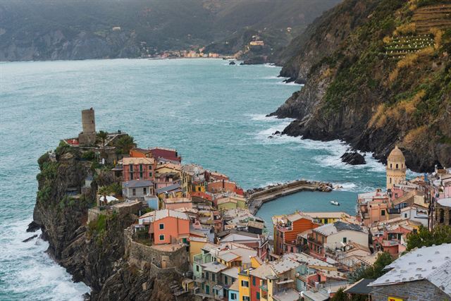 Aerial view of Vernazza with its Doria castle tower, tiny harbor and pastel houses on a rocky headland