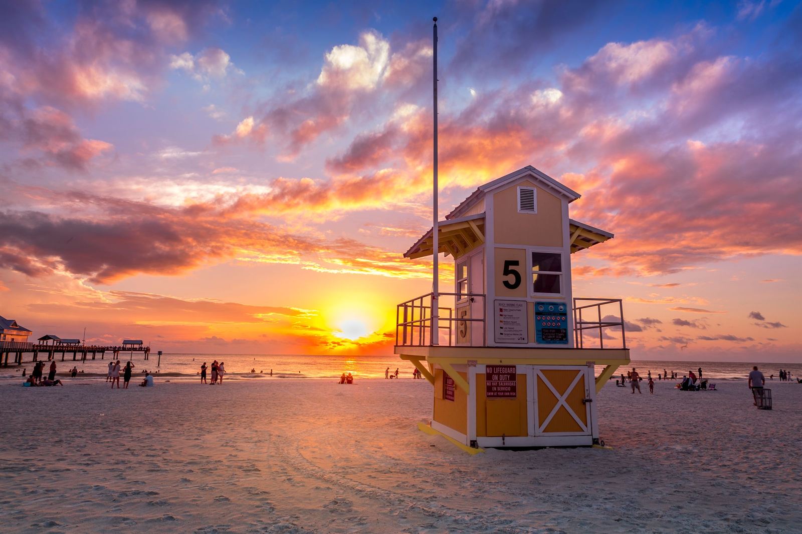 Lifeguard tower 5 on Clearwater Beach silhouetted against a blazing orange sunset, with Pier 60 behind