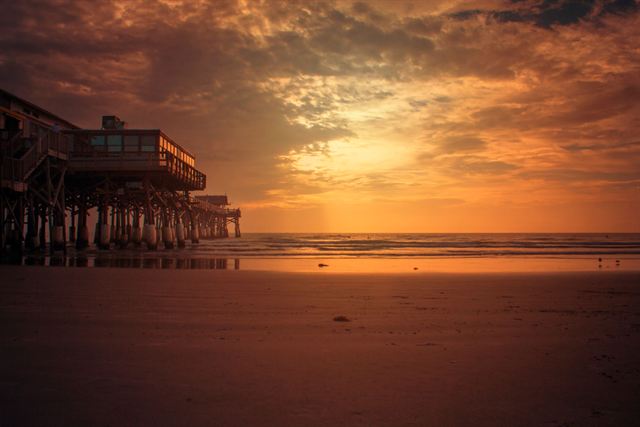 Cocoa Beach Pier silhouetted against a golden sunrise over calm ocean and wet sand