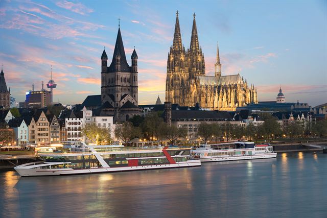 Cologne Cathedral and Great St. Martin Church lit at dusk above the Rhine riverfront