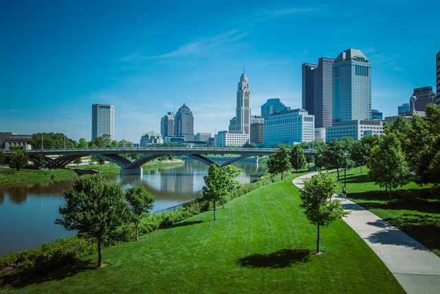 Columbus Ohio downtown skyline beyond the Scioto River, a stone arch bridge and green riverfront park