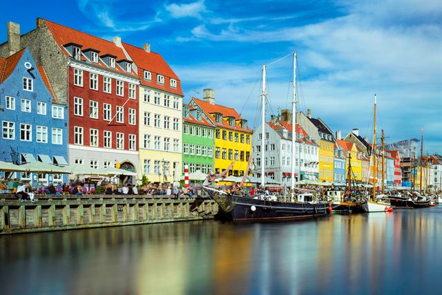 Nyhavn canal in Copenhagen with colorful gabled townhouses, cafes and moored wooden ships