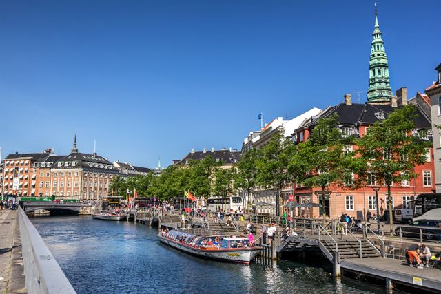 Canal tour boat passing Copenhagen waterfront buildings and a green copper church spire