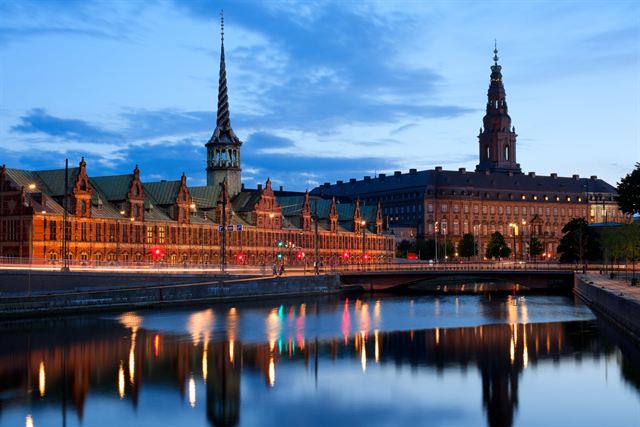Christiansborg Palace and the Stock Exchange spire in Copenhagen reflected in a canal at dusk