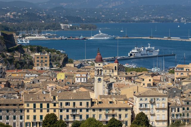 Corfu Town rooftops and St. Spyridon bell tower above the harbor with ferries and cruise ship