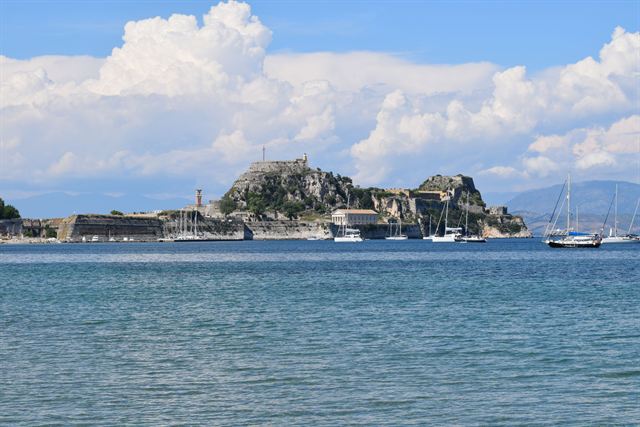 Old Fortress of Corfu on its rocky promontory with sailboats offshore under white clouds