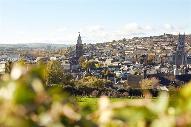Cork city skyline of hillside houses, Shandon bell tower and church spires beyond greenery