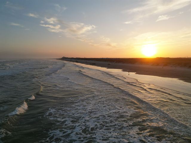 Gulf waves rolling onto a long sandy Corpus Christi beach under a glowing sunset sky