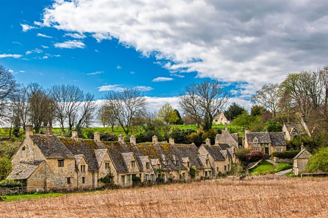 Arlington Row weavers' cottages in Bibury, a row of Cotswold stone houses under blue sky