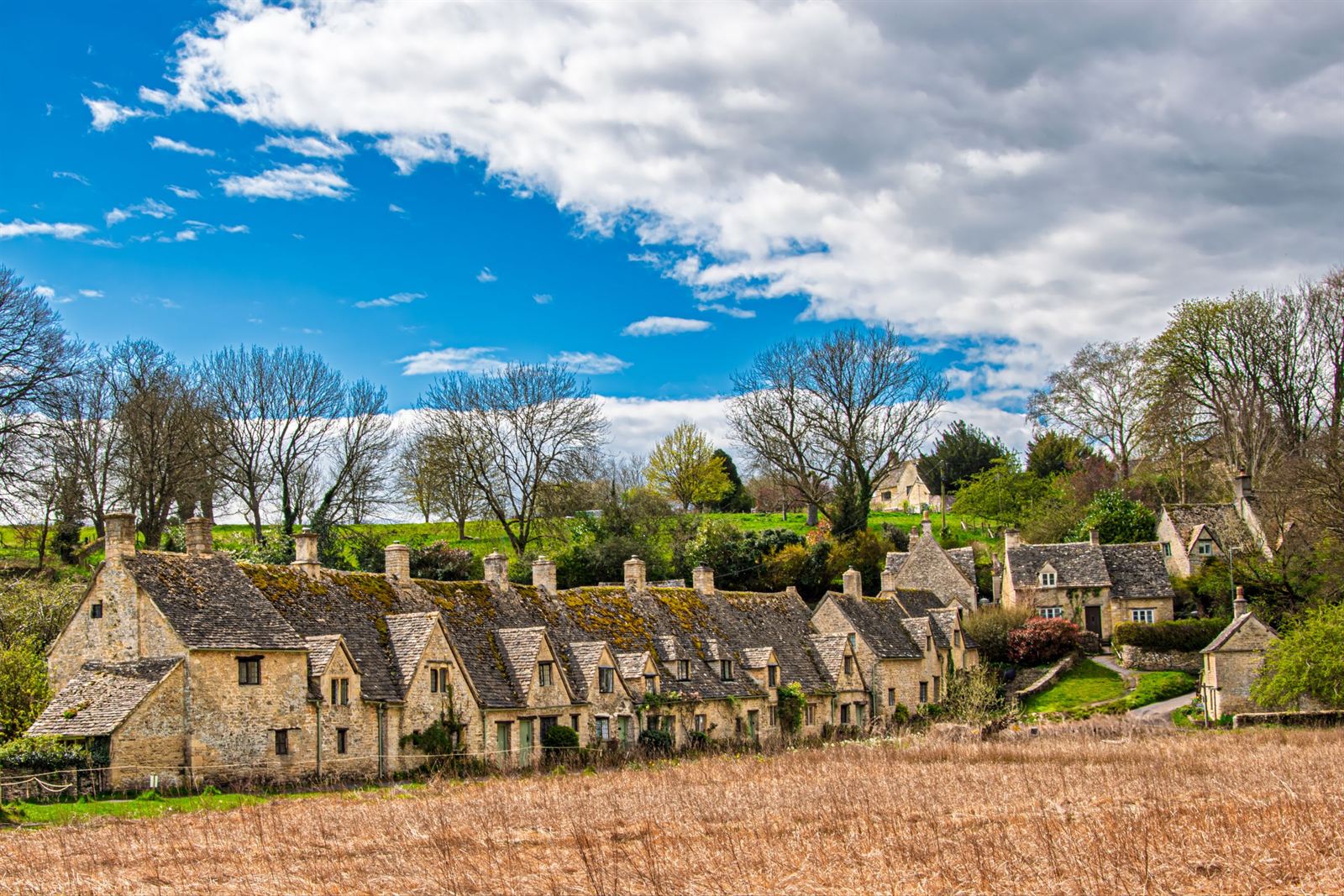 Arlington Row weavers' cottages in Bibury, a row of Cotswold stone houses under blue sky