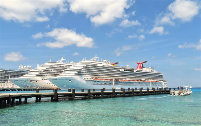 Two Carnival cruise ships docked at a long pier over clear turquoise water in Cozumel