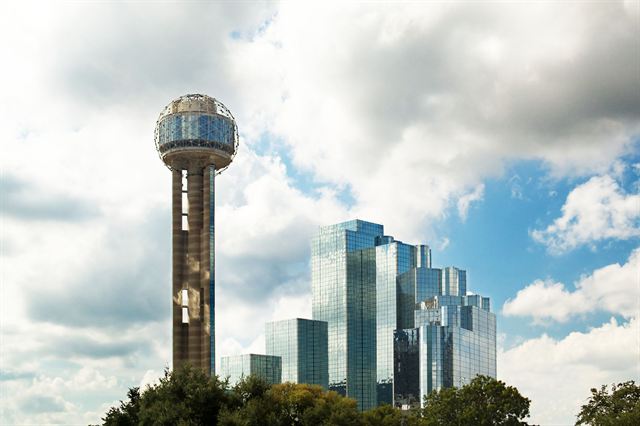 Reunion Tower's lit sphere beside the reflective Hyatt Regency towers in Dallas against white clouds