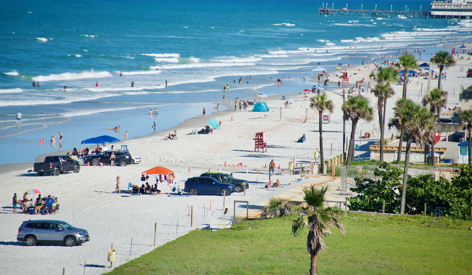 Cars parked on the hard-packed sand of Daytona Beach, with beachgoers and the pier behind