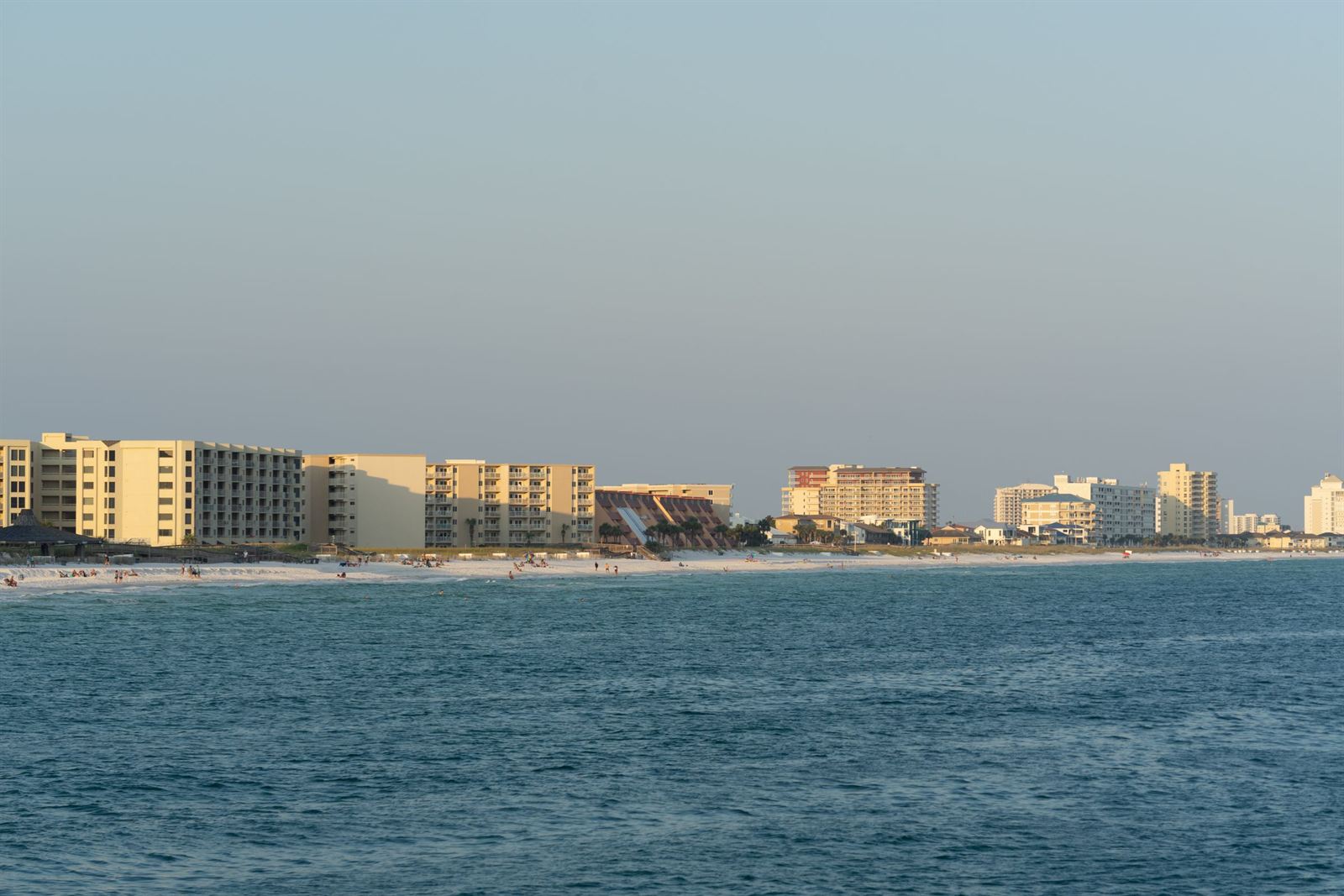 Row of Destin beachfront condos and resorts along the Gulf shore at dusk across calm water