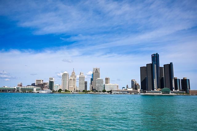 Detroit skyline and Renaissance Center towers across the turquoise Detroit River under a blue sky