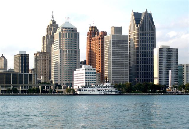 Downtown Detroit skyscrapers along the Detroit River waterfront with a white riverboat docked in front