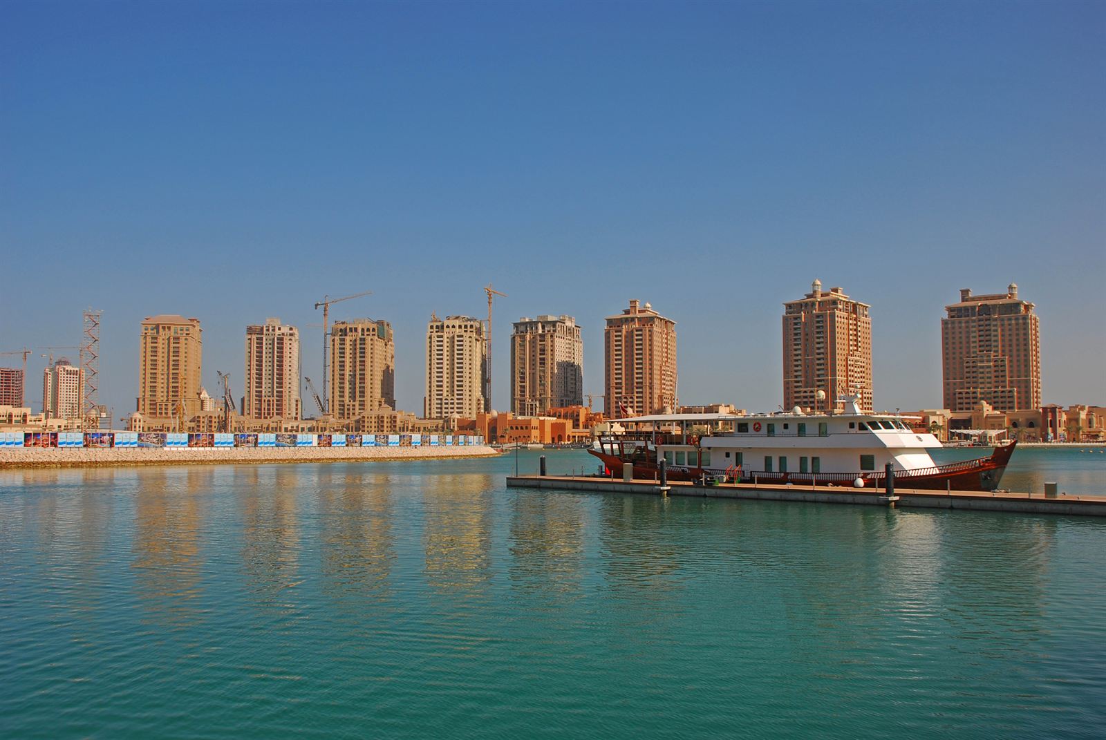 Row of tan residential towers along the marina at The Pearl-Qatar in Doha with a docked boat