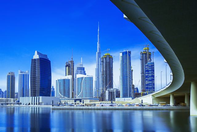 Business Bay towers and Burj Khalifa reflected in the Dubai creek extension under blue sky
