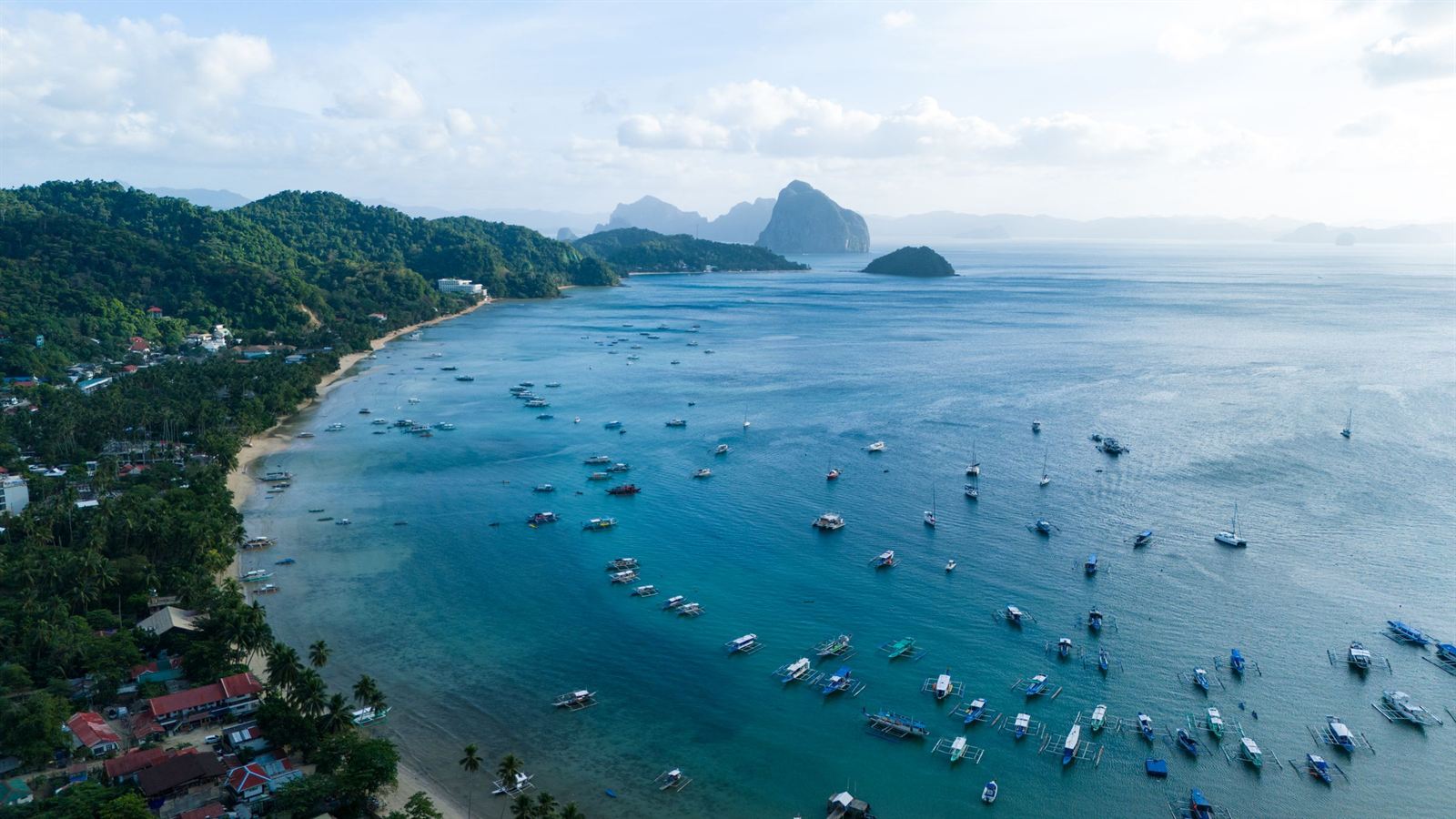 Aerial view of El Nido's Bacuit Bay with bangka boats, beachfront town and limestone islands