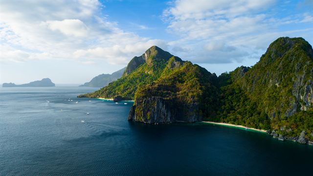 Aerial view of a jungle-covered limestone island rising from deep blue water off El Nido