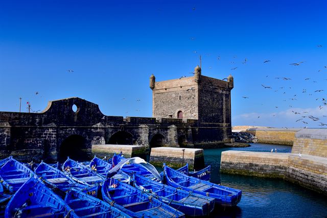 Blue fishing boats in Essaouira port below the stone Skala du Port tower and sea wall