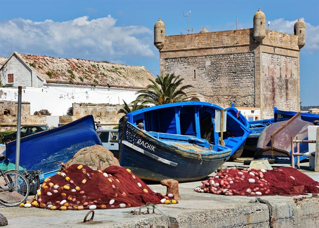 Blue fishing boats and red nets on the quay in front of the stone fort tower in Essaouira