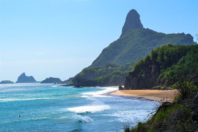 Pointed Morro do Pico peak above a curving beach and turquoise surf in Fernando de Noronha