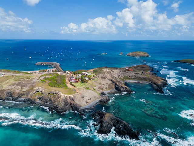 Aerial view of a rocky Fernando de Noronha islet with surf and deep blue Atlantic water