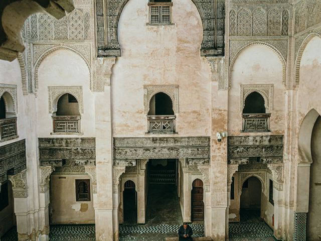 Carved stucco and cedar-wood arches around a historic madrasa courtyard in Fez