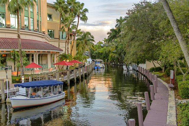 Water taxi docked along a palm-lined canal walkway beside a restaurant